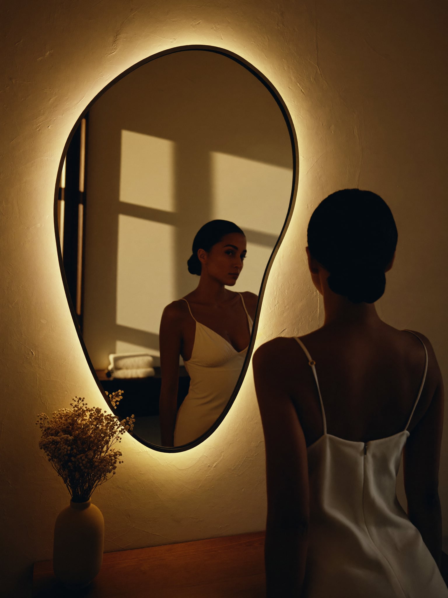 Woman looking into a backlit organic mirror in a warm dressing area at DK Aesthetics in Highland Park, IL